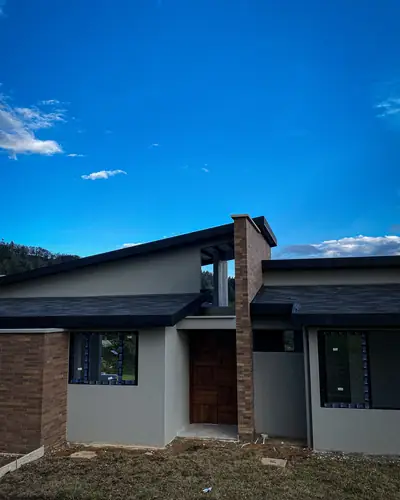 Casa campestre terminada con fachada en ladrillo, cubierta oscura y ventanería negra