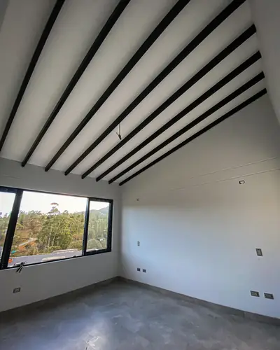 Habitación con techo inclinado, vigas a la vista y ventana panorámica